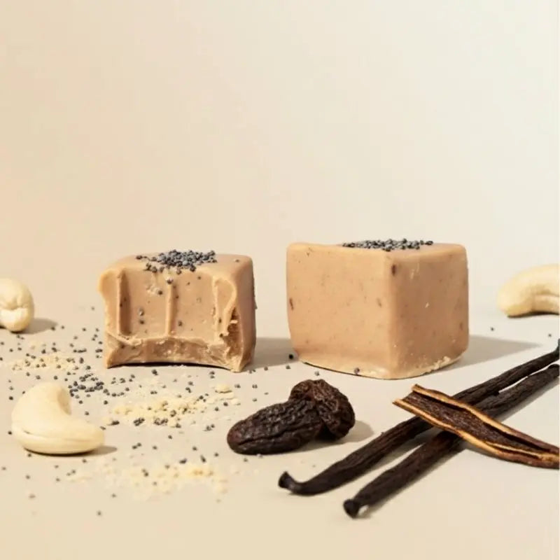 Zwei Tonka Mohn Pralinen von Belly Love in Nahaufnahme – zuckerfrei, clean label und reich an Ballaststoffen, gesüßt mit Erdmandel, Yaconwurzel und Datteln, verfeinert mit Vanille und Mohn, umhüllt von unserer blonden Schokolade (wie weiße Schokolade). Vegan, ohne glutenhaltige Zutaten und bio.