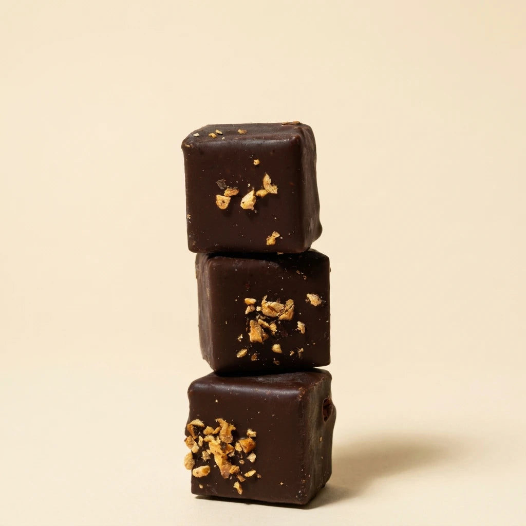 Belly Love Pecan Crunch Pralinés Close-up – gestapelte dunkle Schokoladenkuben mit goldenen Pecan-Stücken, bio und industriezuckerfrei